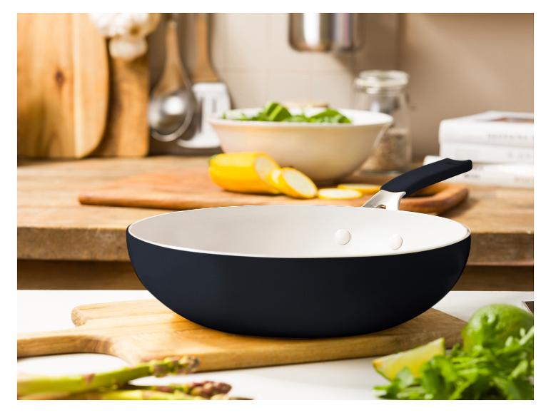 Eine schwarze Pfanne mit weißer Innenseite auf einer Küchenarbeitsplatte mit Gemüse.