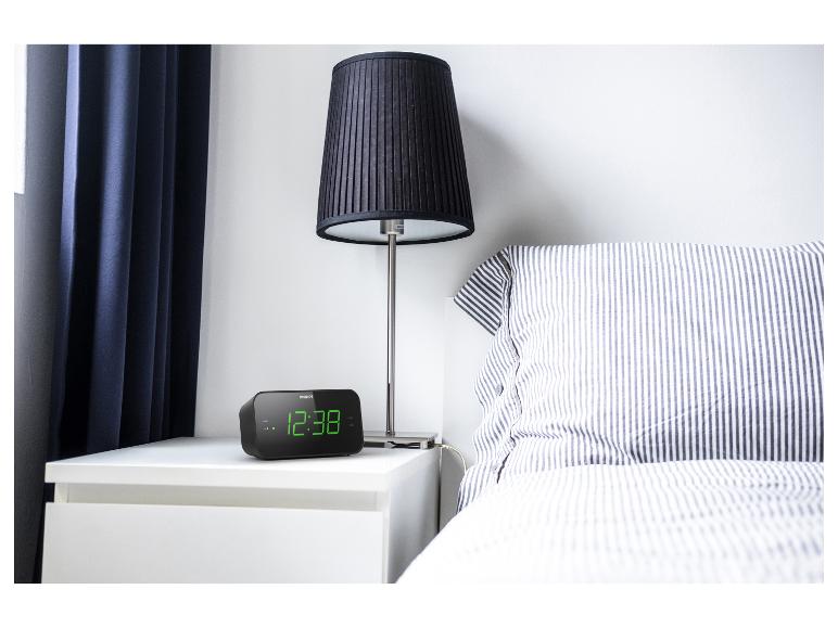 Philips Wecker mit grünen Ziffern auf einem weißen Nachttisch neben einem Bett.