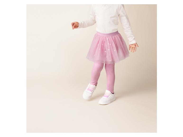 Ein Mädchen trägt einen rosa Tüllrock, Leggings und weiße Sneakers.