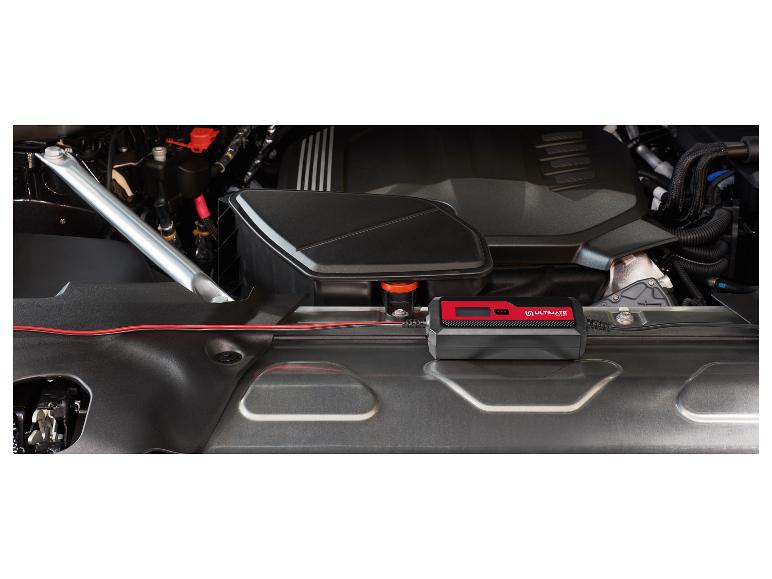 Batterieladegerät mit roten Kabeln im Motorraum eines Autos angeschlossen.