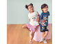 Zwei lächelnde Kinder in Sommerpyjamas mit Welpenmotiven, vor hellblauem Hintergrund und Holzboden.