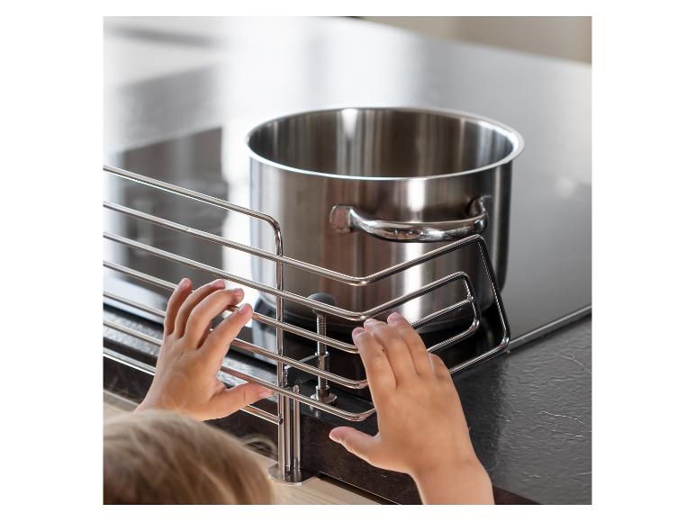 Kinderhände berühren den Metallschutz des Herdes, der vor dem heißen Topf schützt.