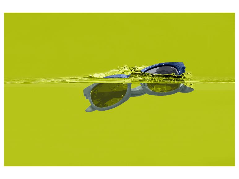 Blaue Sonnenbrille schwimmt in gelbem Wasser mit Spritzern.