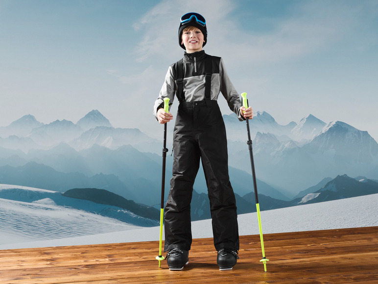 Ein Junge in Skiausrüstung mit Skistöcken, bereit zum Skifahren.