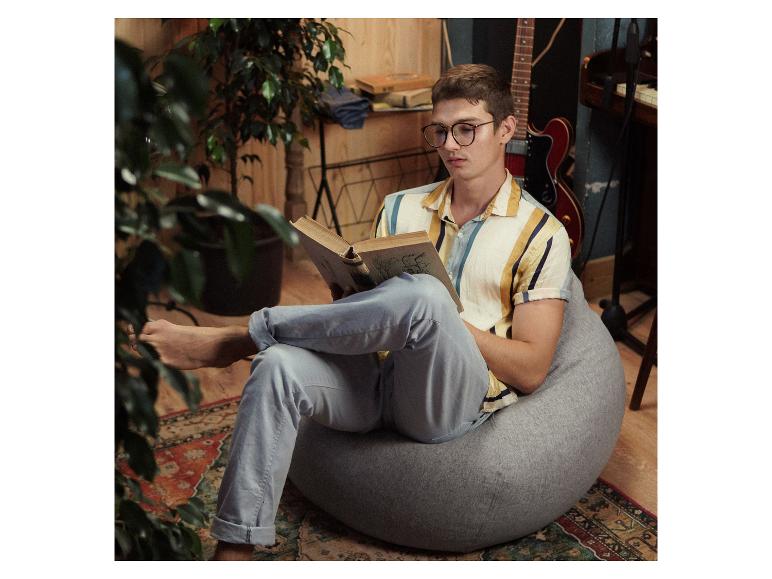 Ein Mann liest ein Buch in einem grauen Sessel.