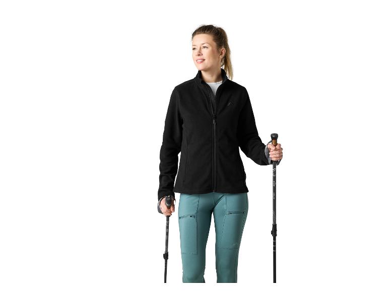 Frau in schwarzer Fleecejacke und türkiser Hose, Trekkingstöcke haltend.