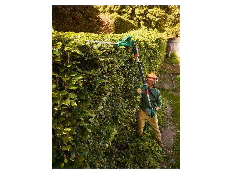 Frau schneidet Hecke mit Langstiel-Heckenschere, trägt Schutzhelm und Brille.