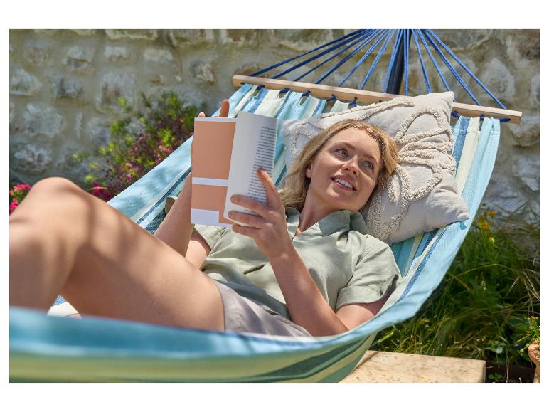 Frau entspannt in einer Hängematte mit einem Buch im Garten.