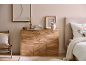 Holzkommode mit Schubladen und Türen, dekoriert mit Vasen und Bildern, neben einem Bett.
