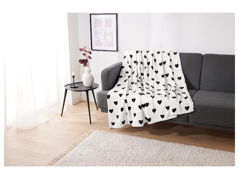 Eine weiße Decke mit schwarzen Herzen auf einem grauen Sofa.