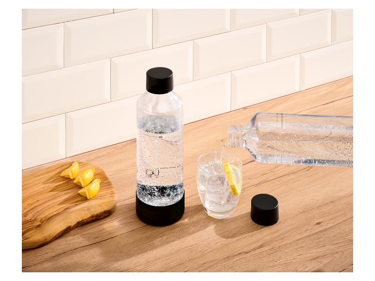 Sprudelwasserflasche und Glas mit Eis und Zitrone auf einer Holztheke.