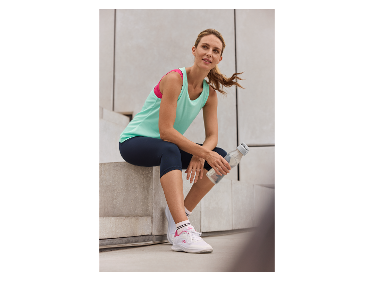 Frau in Crivit Sportkleidung ruht sich auf einer Treppe mit Wasserflasche aus.