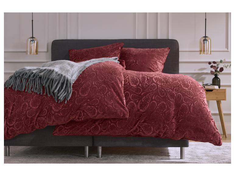 Ein Bett mit roter Paisley-Bettwäsche, einem grauen Überwurf und zwei Pendelleuchten in einem Schlafzimmer.