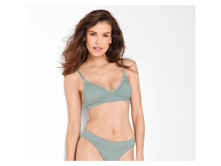 Frau in grünem BH und Slip, mit offenen Haaren, lächelt in die Kamera.