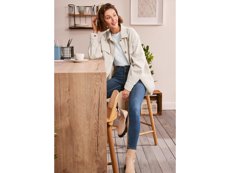 Eine Frau trägt ein hellblaues T-Shirt, eine weiße Jacke und blaue Skinny Jeans.