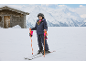 Mädchen in Skijacke, Skihose, Helm und Skihandschuhen auf einer verschneiten Piste.