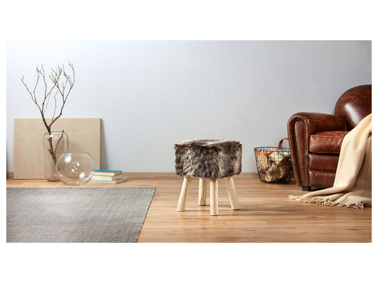 Ein Fellhocker mit Holzbeinen in einem modernen Wohnzimmer.