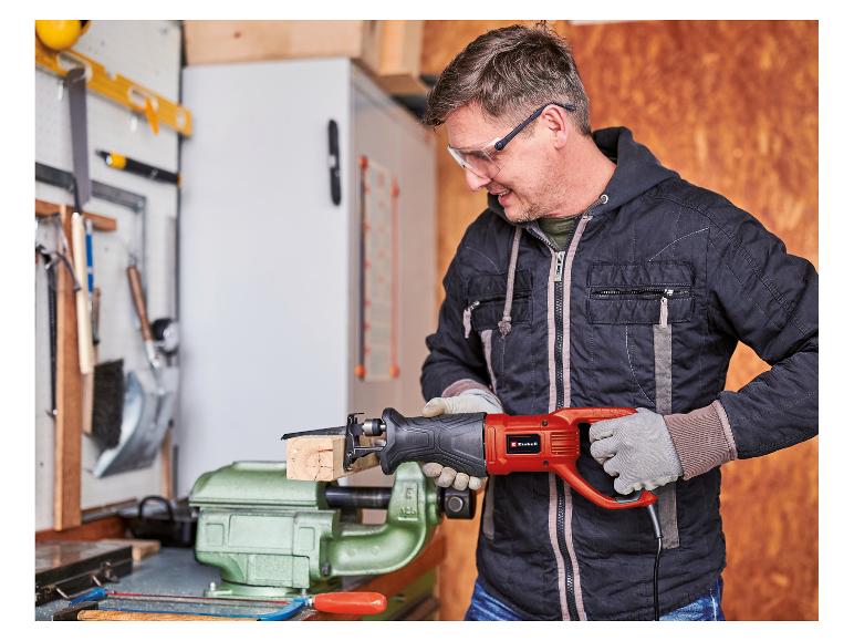 Mann mit Schutzbrille und Handschuhen benutzt eine Säbelsäge, um ein Stück Holz zu schneiden.