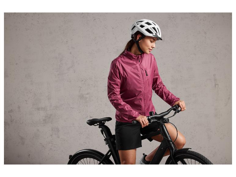 Eine Frau in einer rosa Jacke und einem Fahrradhelm auf einem schwarzen Fahrrad
