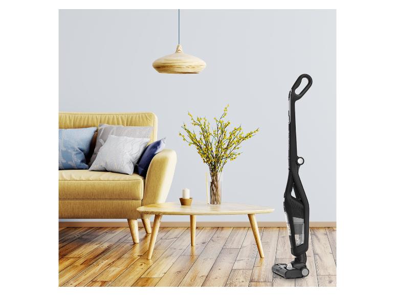 Schwarzer Stielstaubsauger in einem modernen Wohnzimmer mit gelbem Sofa und Holztisch.