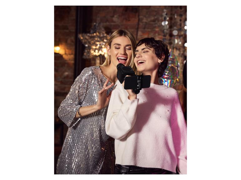 Zwei Frauen singen Karaoke mit Mikrofon und Smartphone auf einer Party.