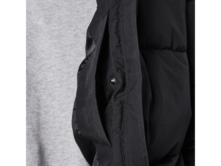 Detail einer schwarzen Steppjacke mit Seitentasche und Druckknopf.