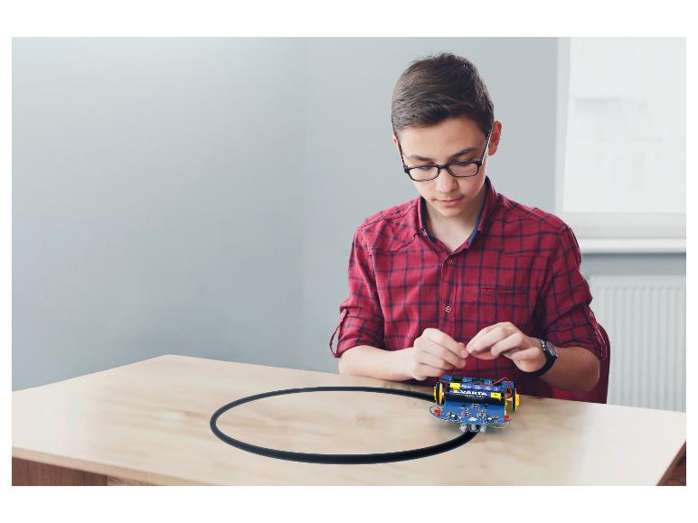 Junge baut einen VARTA-betriebenen Roboter auf einem Tisch mit schwarzer Spur zusammen.