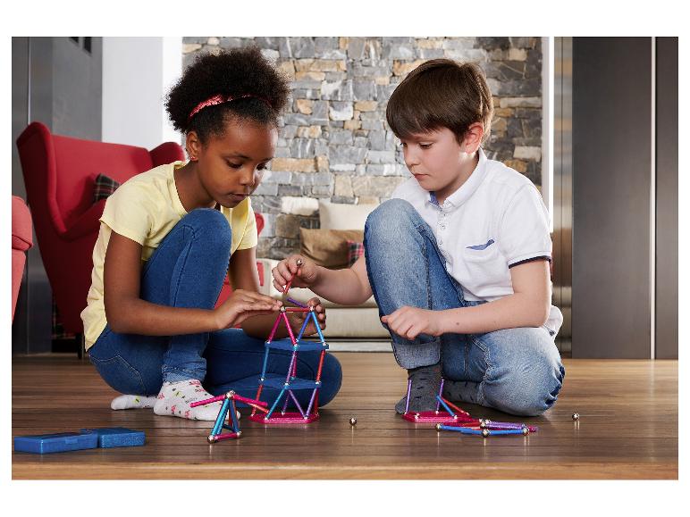 Zwei Kinder spielen mit magnetischem Konstruktionsspielzeug auf einem Holzboden.