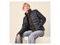 Frau in schwarzer Steppjacke und Jeans, sitzend und lächelnd.