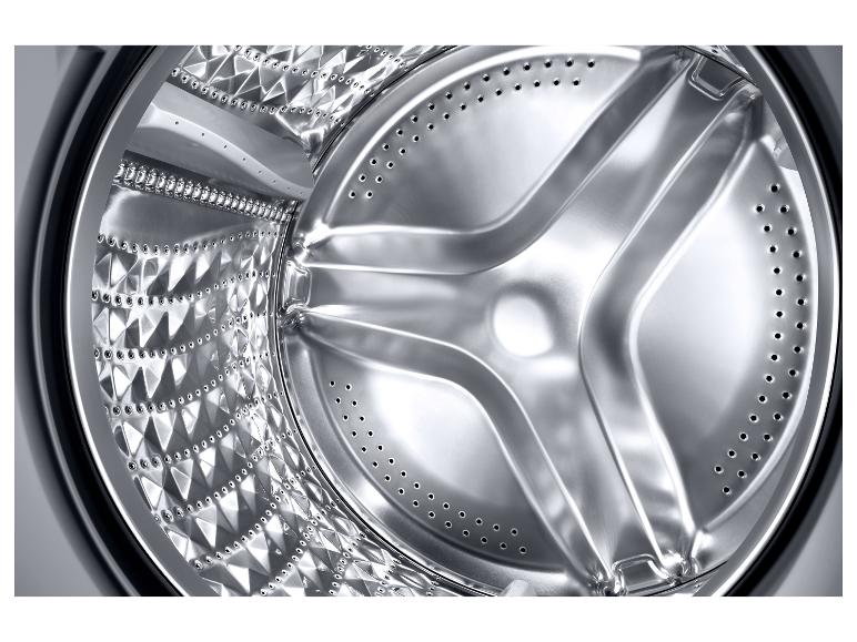 Glänzendes Metallinterieur einer Waschmaschine, mit der texturierten und perforierten Trommel.