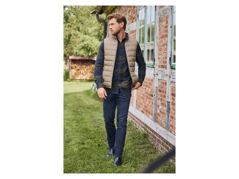 Mann in beiger Steppweste, kariertem Hemd und Jeans geht draußen spazieren.