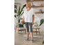 Frau in weißem T-Shirt und grauen Capri-Leggings, mit geflochtener Tasche, steht in einem gemütlichen Raum.