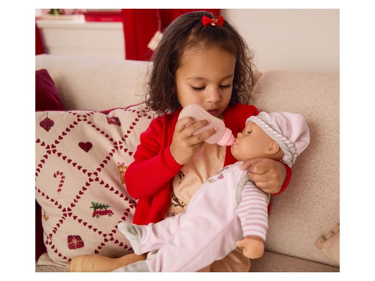 Ein junges Mädchen füttert eine Babypuppe mit einer Flasche auf einem Sofa.