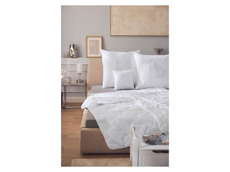 Weiße Bettdecke und Kissen auf einem beigen Bett in einem Schlafzimmer mit Holzboden.