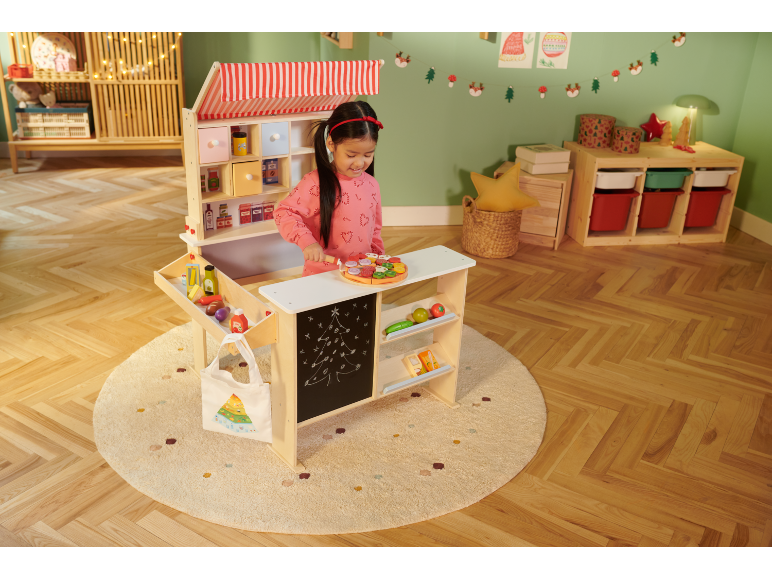 Mädchen spielt mit einem Holzspielzeugladen, weihnachtlich dekoriert.