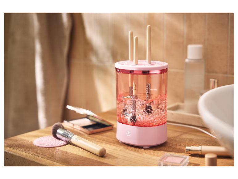 Rosa Make-up-Pinselreiniger mit Pinseln darin, auf einer Holztheke.