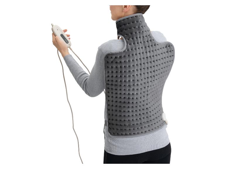 Frau trägt ein graues Heizkissen für Rücken und Nacken und hält eine Fernbedienung.