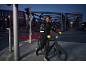 Mann in Steppjacke und Sporthose mit Handschuhen und Helm schiebt nachts ein Fahrrad.