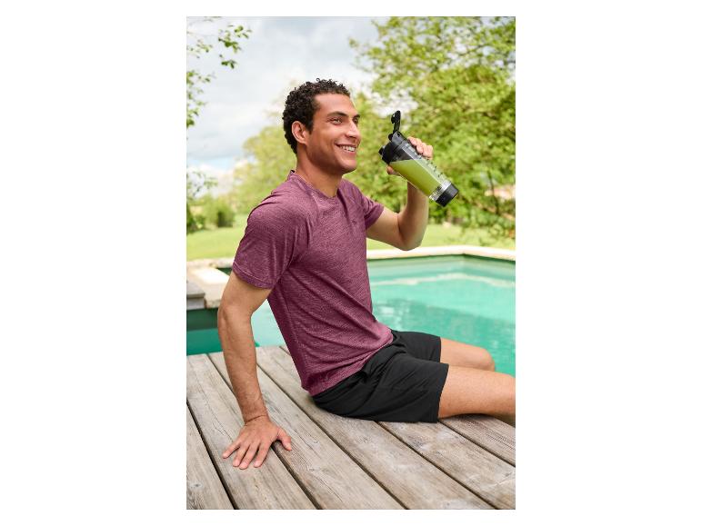 Mann in CRIVIT Funktionsshorts sitzt mit einem Getränk am Pool.