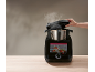 Schwarze smarte Küchenmaschine mit Touchscreen, Dampf steigt auf, eine Hand öffnet den Deckel.