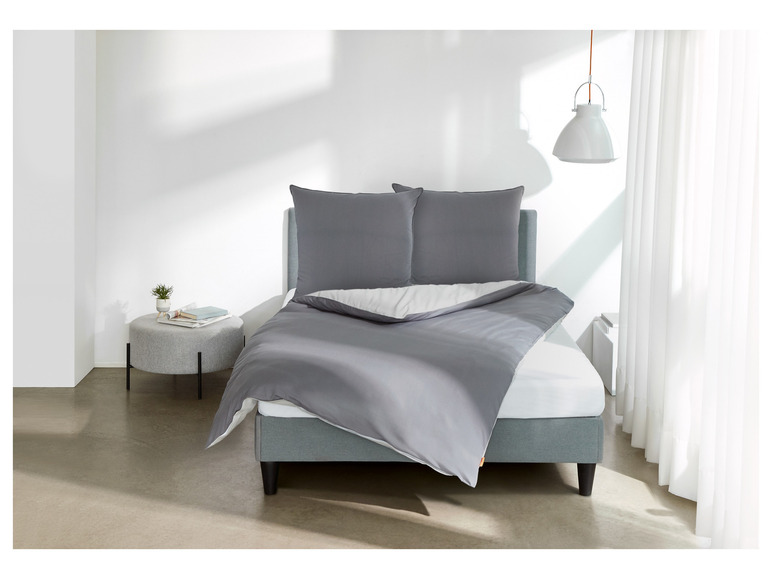 Ein grauer Bettbezug und Kissen auf einem Bett mit einem weißen Laken.