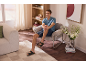 Mann in Shorts und Sandalen, sitzt in einem Sessel in einem modernen Wohnzimmer.