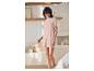 Lächelnde Frau in hellrosa Pyjama, T-Shirt und Shorts, in einem hellen Schlafzimmer.