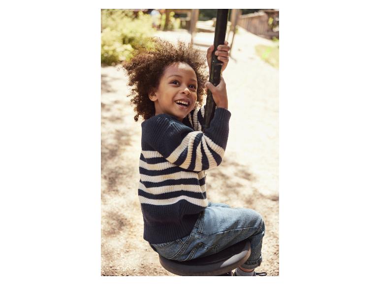 Ein glücklicher Junge in gestreiftem Pullover und Jeans auf einer Schaukel.