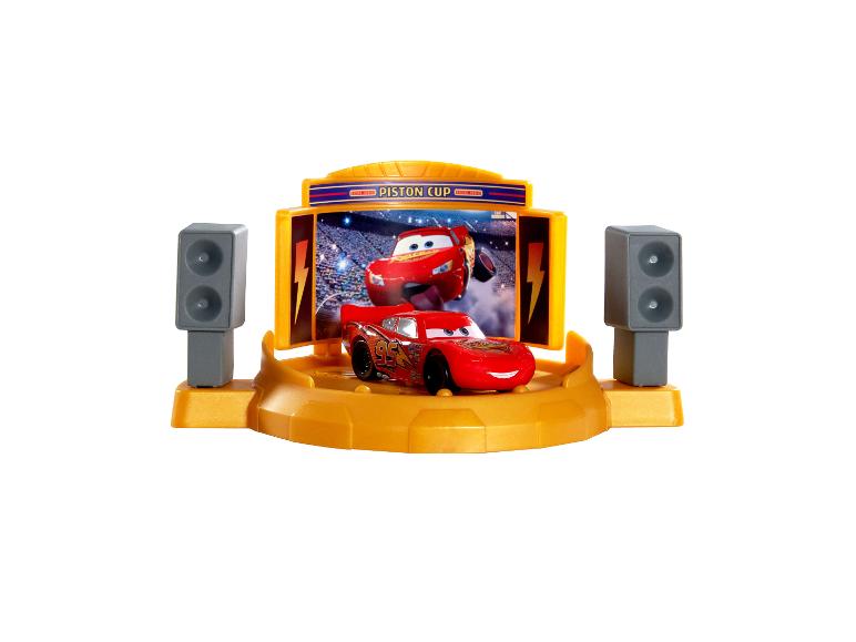 Rotes Spielzeugauto auf einer gelben Bühne mit Bildschirm, der ein anderes Auto und den Text „PISTON CUP“ zeigt.