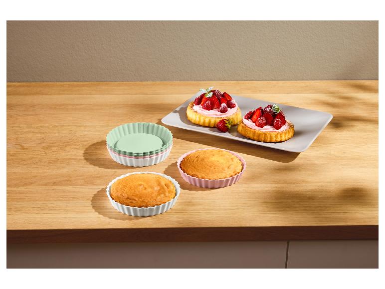 Erdbeertörtchen und Backwaren in Silikonformen auf einem Holztisch.