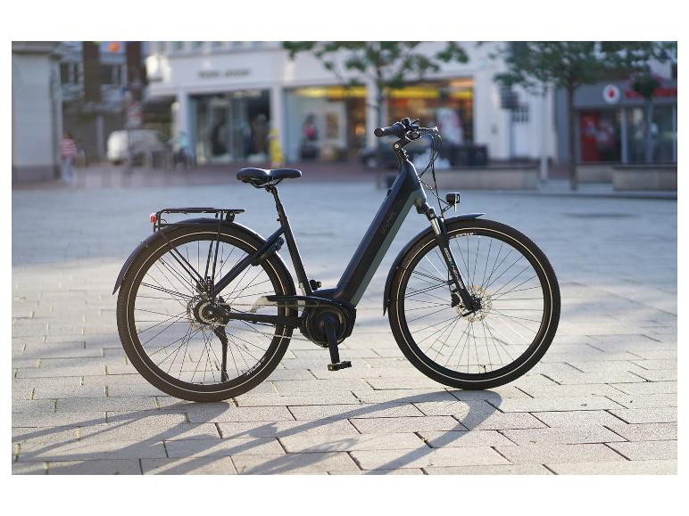 Schwarzes Prophete E-Bike mit Gepäckträger und Schutzblechen, auf einem gepflasterten Stadtplatz geparkt.