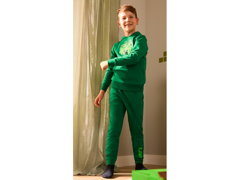 Lächelnder Junge in grünem Kapuzenpullover und Jogginghose mit Monster-Print.