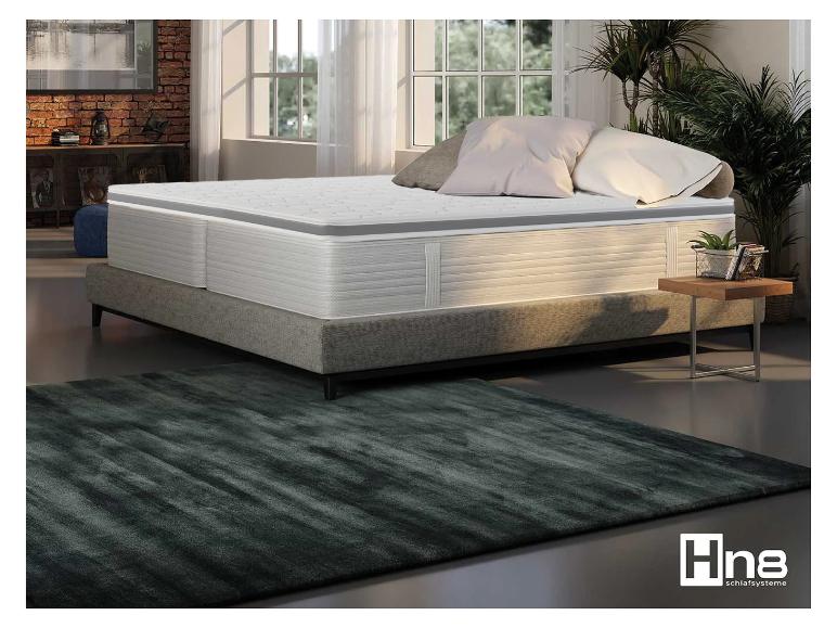 Eine Hn8 Schlafsysteme Matratze und Bettgestell in einem Schlafzimmer mit einem dunkelgrünen Teppich.