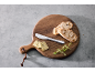 Holzschneidebrett mit Brot, Kräuterbutter, einem Messer und frischen Kräutern.